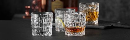Four NACHTMANN Bossa Nova SOF glasses, three of them filled with either Whiskey or other drinks, one of them empty. In the background are liquor bottles.<br/>