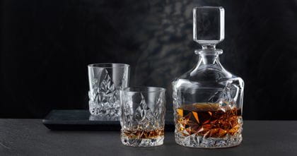 The NACHTMANN Sculpture Whiskey decanter besides the NACHTMANN Sculpture Whiskey tumbler, both of them filled with Whiskey. In the background an empty Sculpture tumbler on a serving tray.<br/>