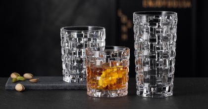 The NACHTMANN Bossa Nova SOF filled with whisky next to the empty Bossa Nova longdrink glass on a black stone sideboard. Behind them the empty Bossa Nova tumbler.<br/>
