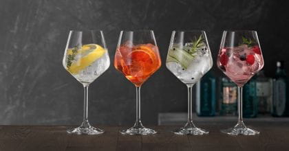 Four SPIEGELAU Gin and Tonic glasses on a wooden table, each of them filled with a different Gin cocktail.<br/>