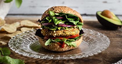Der kleine NACHTMANN Bossa Nova Teller auf einem Tisch, mit einem leckeren Hamburger, umgeben von Salatblättern, Kartoffelchips, Basilikum in einem Blumentopf und einer Avocado.<br/>