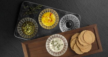 Vier NACHTMANN Bossa Nova Dip-Schalen, drei davon sind mit verschiedenen Dips gefüllt und eine ist leer. Drei Schalen befinden sich auf einer kleinen Glasplatte. Eine gefüllte Schale befindet sich auf einem Holzbrett mit Keksen daneben drauf. <br/>