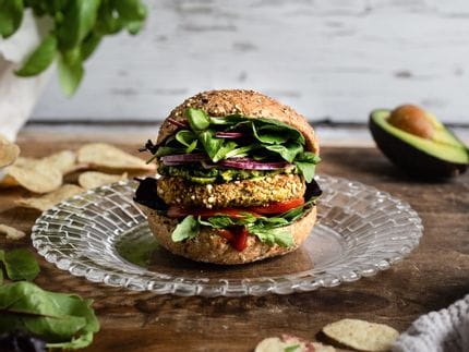 La petite assiette NACHTMANN Bossa Nova avec un savoureux hamburger sur une table, entourée de feuilles de salade, de chips, de basilic dans un pot de fleurs et d'un avocat.<br/>