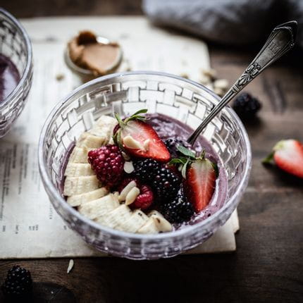Die NACHTMANN Bossa Nova Schale ist mit einem lila Sahne-Smoothie gefüllt, der mit einer in Scheiben geschnittenen Banane, Brombeeren und einer halbierten Erdbeere garniert ist.<br/>