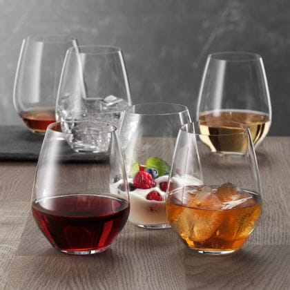 Six gobelets SPIEGELAU Authentis Casual sur une table en bois, chacun rempli différemment. Avec du vin rouge, avec une boisson rafraîchissante sur glace, avec un dessert crémeux, avec du vin blanc, avec de l'eau et des glaçons et avec une liqueur brune.<br/>