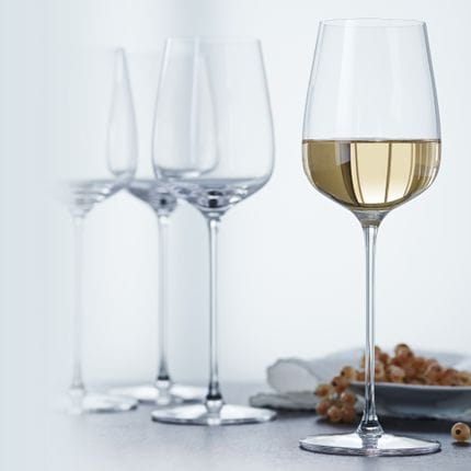Four SPIEGELAU Willsberger Anniversary White Wine glasses, one of them filled with white wine.<br/>