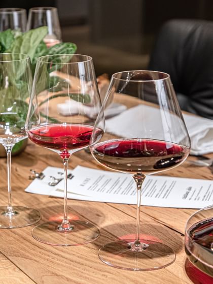 Das mit Rotwein gefüllte SPIEGELAU Definition Burgunderglas und das Bordeauxglas auf einem Holztisch mit einem leeren Universalglas im Hintergrund.<br/>